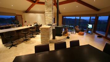 A spacious kitchen with a stone fireplace, large windows, and a high ceiling with wooden beams.