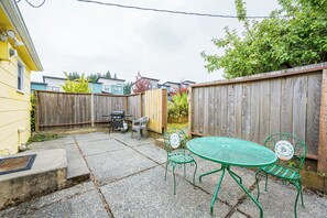 Ein Garten mit Terrassentisch und -stühlen, einem Grill und einem Holzzaun.