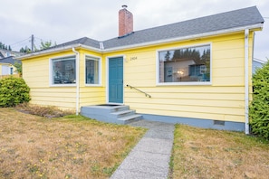 A yellow single-story house with a blue door, numbered 2404, and a small front porch. - Sunny Hills 2-bedroom house in welcoming Port Angeles for your getaway (Port Angeles)