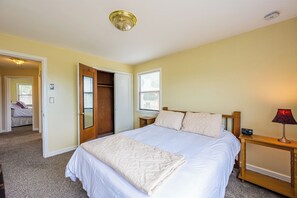 Ein Schlafzimmer mit Bett, Nachttisch, Lampe und einer Tür zu einem anderen Raum.