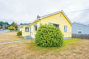 Ein gelbes Einfamilienhaus mit einer Veranda, einem großen grünen Busch und einem Holzzaun im Hintergrund.