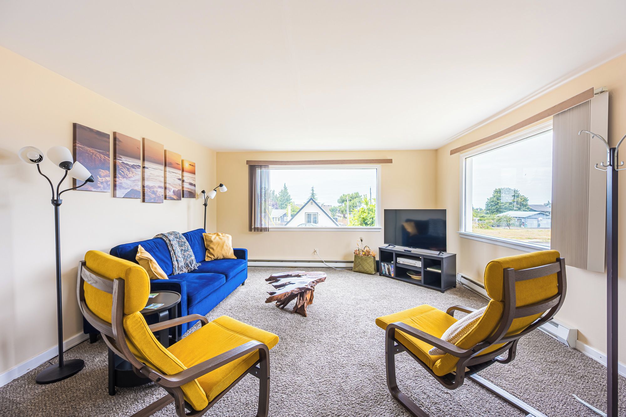 Ein Wohnzimmer mit einem blauen Sofa, gelben Sesseln, einem Fernseher und einem großen Fenster.