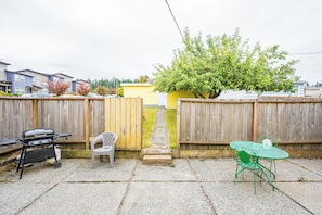 A backyard with a barbecue grill, a green metal table and chair, a white plastic chair, and a wooden fence. - Sunny Hills 2-bedroom house in welcoming Port Angeles for your getaway (Port Angeles)