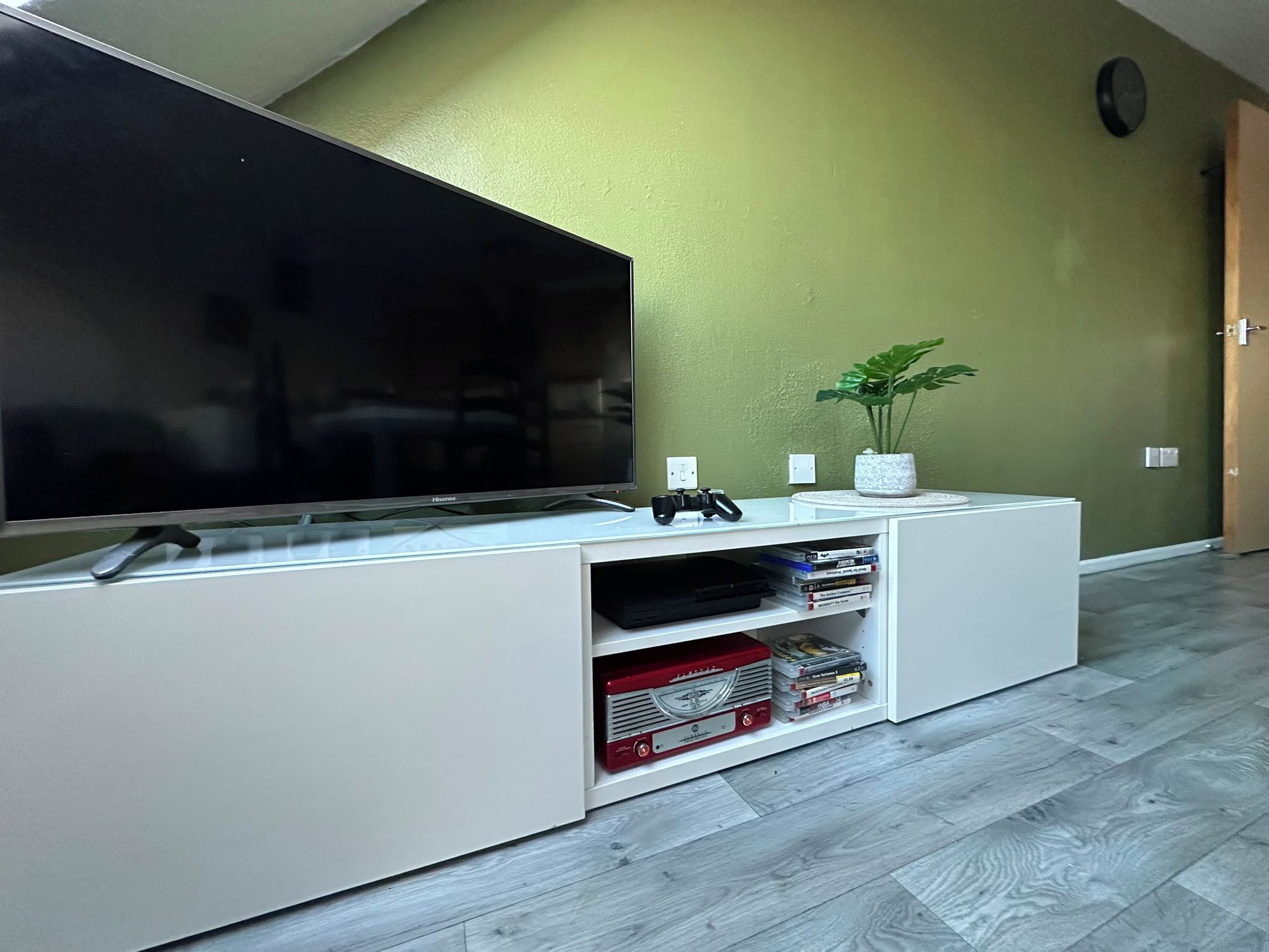 Un mueble blanco de entretenimiento con un televisor de pantalla plana, una planta y un estante con DVDs.