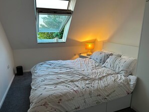 Ein Schlafzimmer mit einem Bett, einem Fenster, einem Nachttisch und einer Lampe.