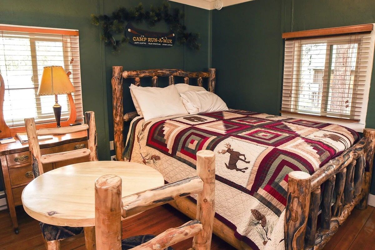 A rustic bedroom with a wooden bed, a round table, and a lamp.