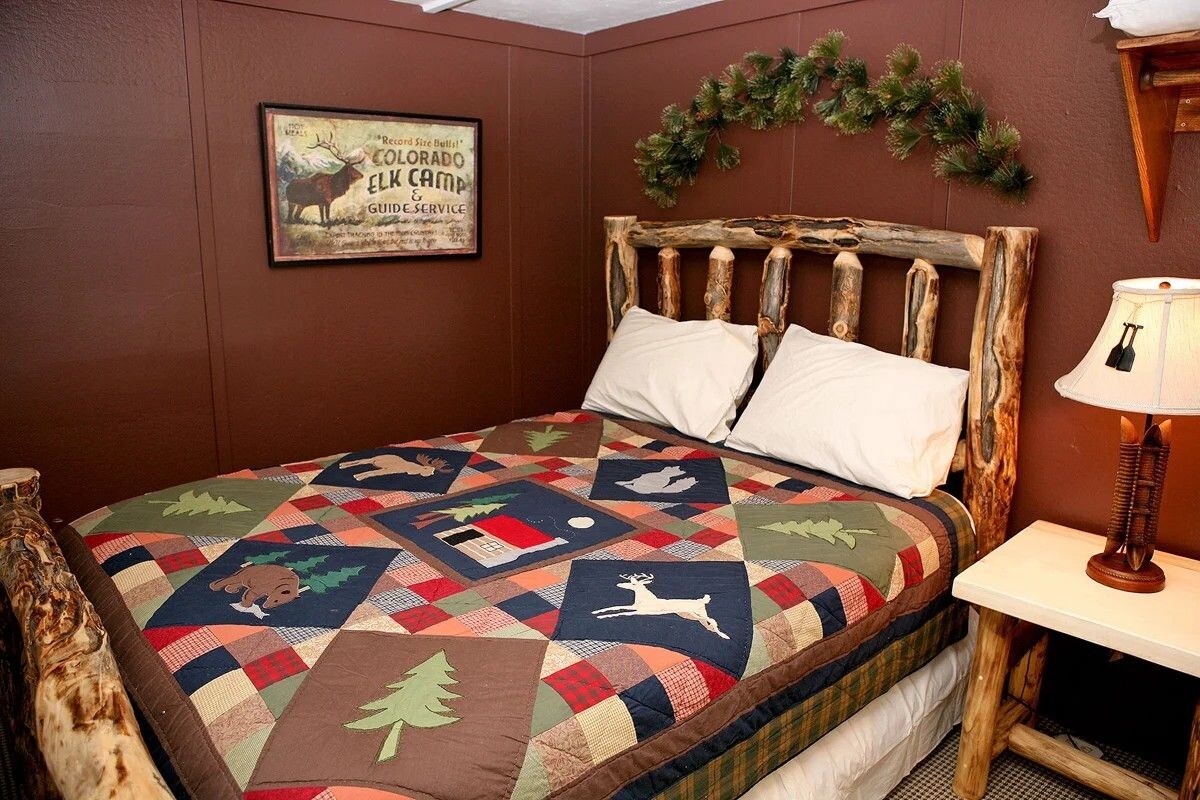 A bed with a quilt featuring animal prints, a wooden headboard, a framed sign on the wall, and a small table with a lamp.