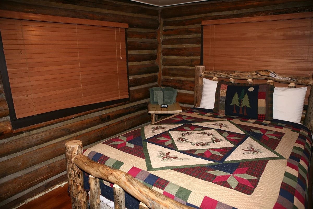 A log cabin bedroom with a large bed, a wooden headboard, and a quilt with a geometric pattern.