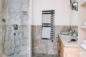 Un baño con cabina de ducha de vidrio, toallero, lavabo con artículos de aseo y mueble de madera.