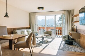 Una sala de estar moderna con sofá, mesa de comedor y mesa de centro. Hay un balcón con vistas a montañas.