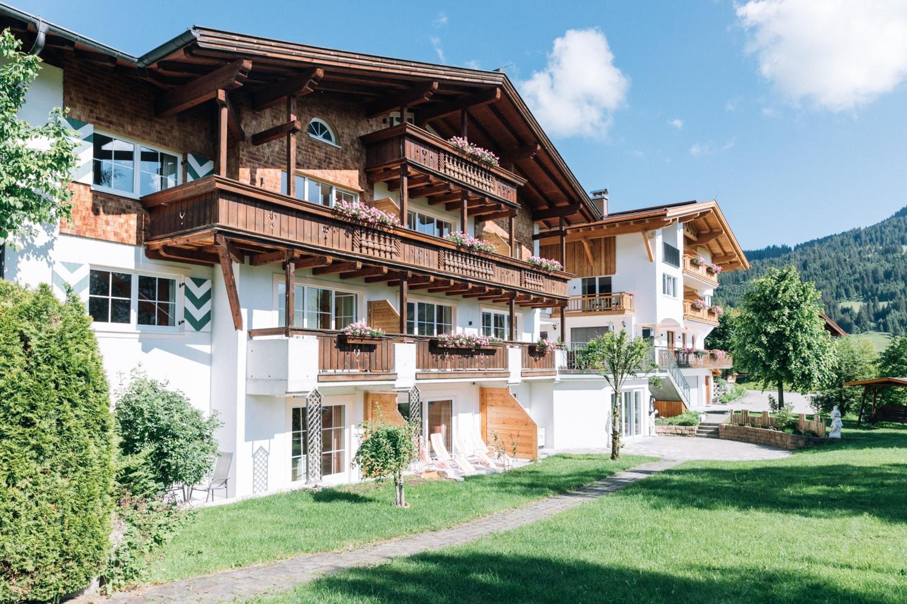 A multi-story building with wooden balconies, a stone facade, and a clear view of the surrounding greenery and hills.