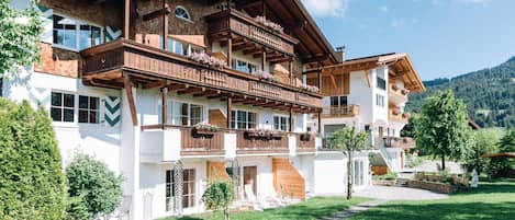 A multi-story building with wooden balconies, a stone facade, and a clear view of the surrounding greenery and hills.