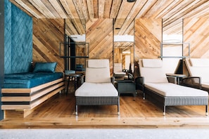 Un interior moderno con techo de madera, un sofá, dos sillas, una mesita y un espejo.
