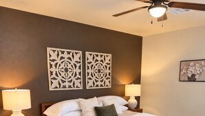 Ein Schlafzimmer mit Bett, Nachttischlampen, dekorativen Wandverkleidungen, einem Deckenventilator und Teppichboden.