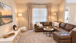 Ein Wohnzimmer mit braunem Ledersofa, einem weißen Beistelltisch, einem runden Couchtisch und einer Lampe.