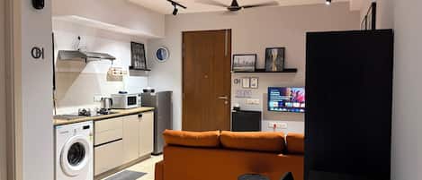 A compact living space with a kitchenette, a sofa, a television, and a ceiling fan.