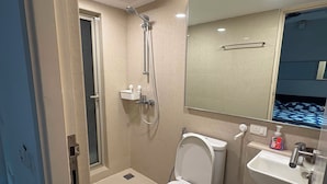 Un baño con inodoro, lavamanos, espejo, ducha y un ventanal pequeño.