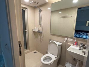 Een badkamer met toilet, wastafel, spiegel, douche en een klein raam.