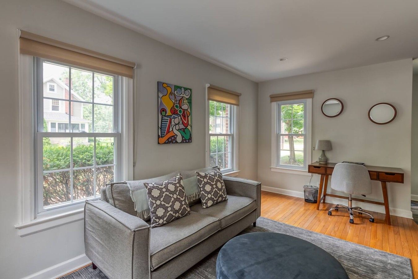 A living room with a sofa, a desk, and two windows.