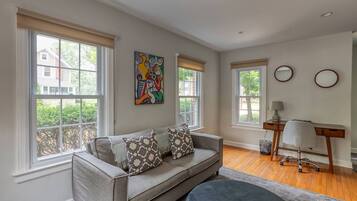 A living room with a sofa, a desk, and two windows.