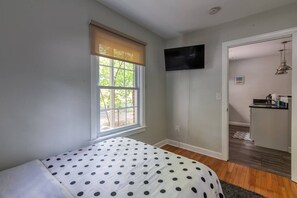 Un dormitorio con cama, ventana con persianas, televisor en la pared y pequeña zona de kitchenette.