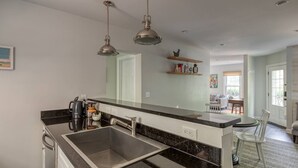 Een moderne keuken met een zwart aanrecht, een roestvrijstalen spoelbak en hangende verlichting.