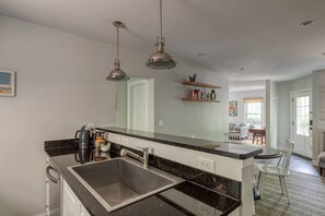 Una cocina moderna con encimera negra, pileta de acero inoxidable e iluminación colgante.