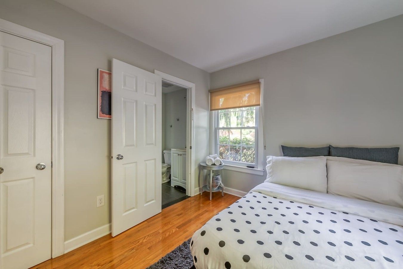A bedroom with a bed, a window with blinds, a door, and a small table with towels.