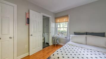 A bedroom with a bed, a window with blinds, a door, and a small table with towels.