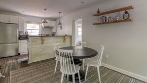Een moderne keuken met witte kasten, een centraal eiland, hanglampen, en een eethoek met een ronde tafel en stoelen.