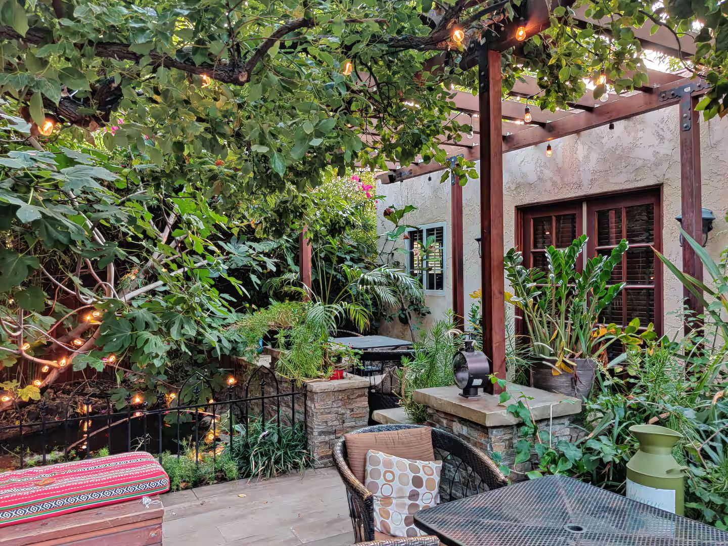 Une terrasse extérieure avec une table, des chaises et une pergola décorée de guirlandes lumineuses.