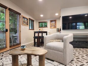Ein Wohnzimmer mit einem grauen Sessel, einem Holztisch, einem Fernseher und einem Essbereich mit Tisch und Stühlen.