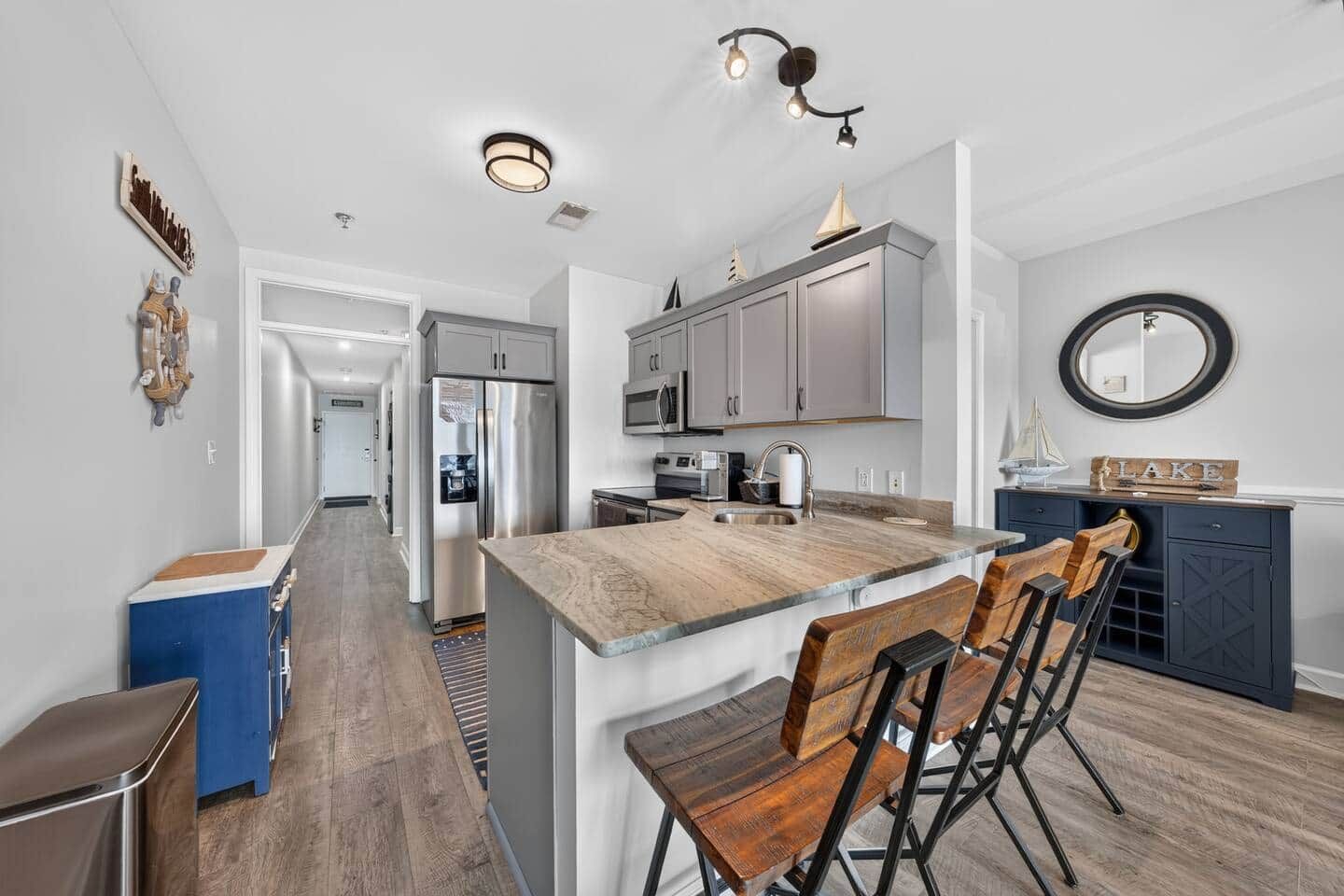 A modern kitchen with a central island, stainless steel appliances, and a dining area with wooden chairs.