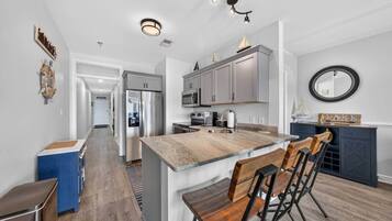 A modern kitchen with a central island, stainless steel appliances, and a dining area with wooden chairs.