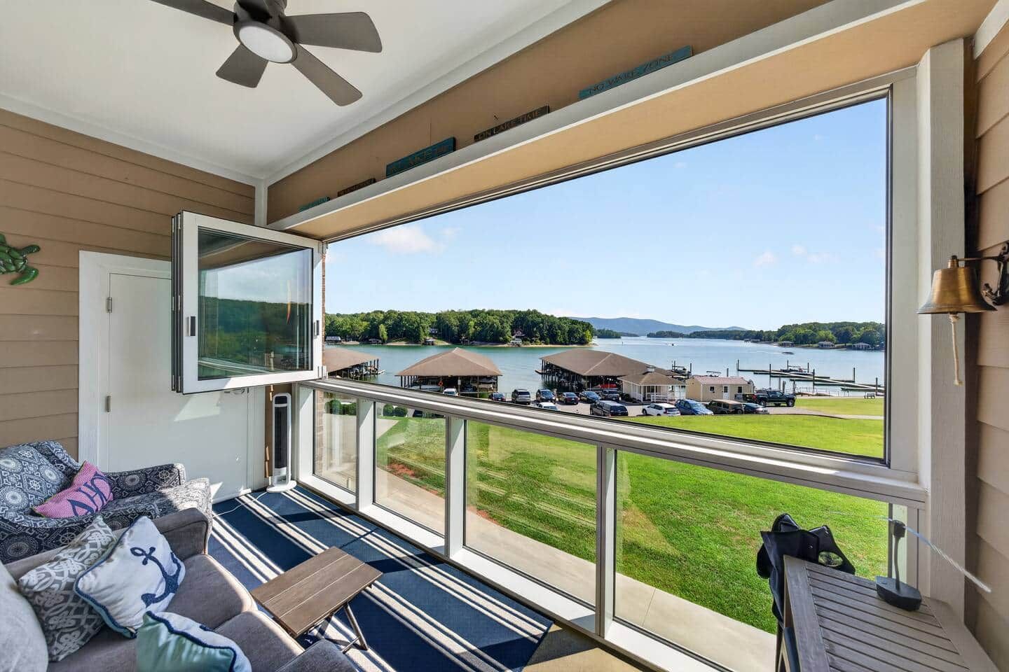 A balcony with a view of a lake, a seating area with patterned cushions, and a ceiling fan.