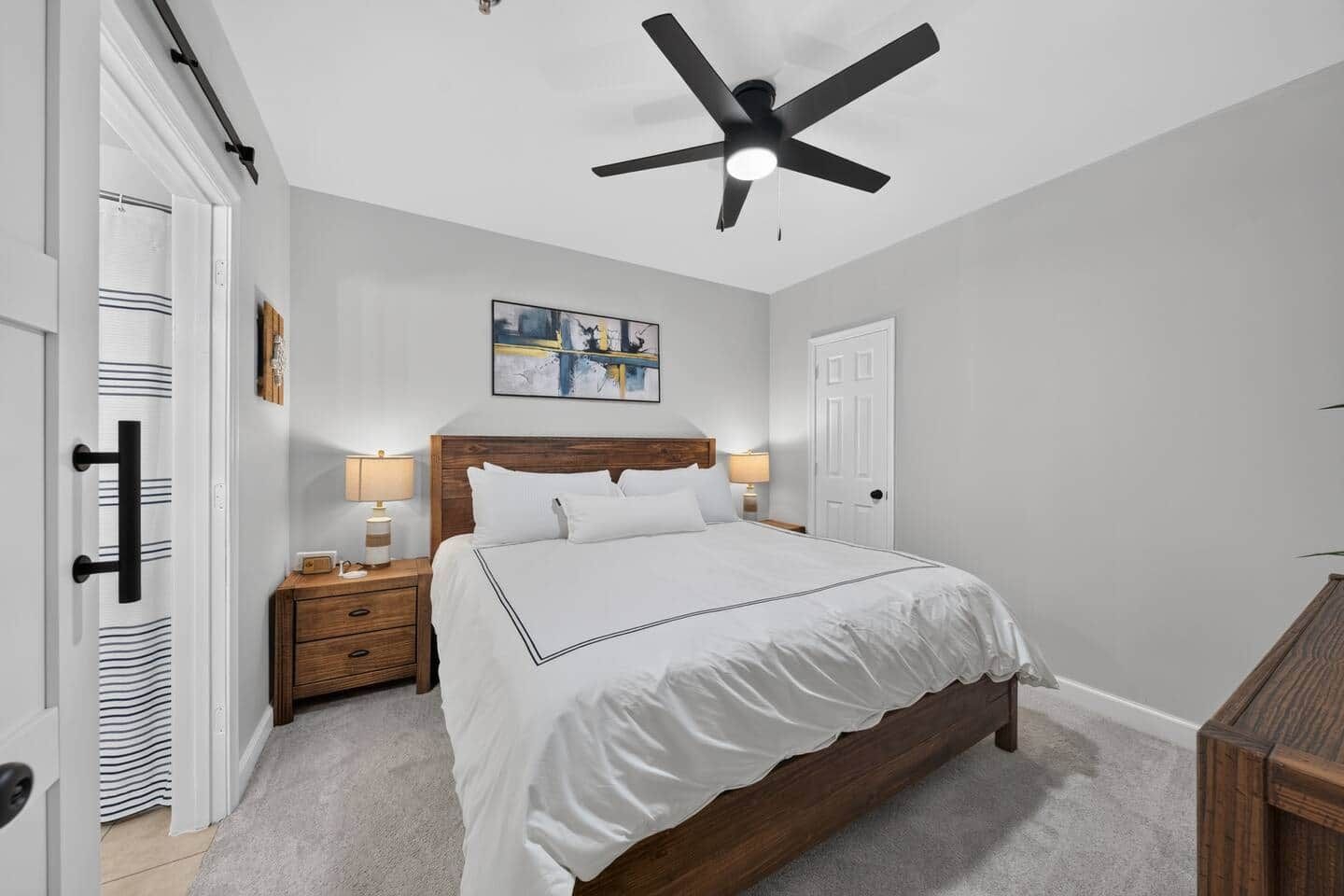A bedroom with a bed, bedside tables, a ceiling fan, and a door.