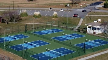 An outdoor tennis court complex with multiple courts, a parking area, and a small building.