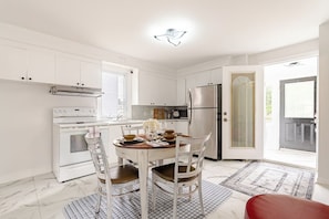 A modern kitchen with white cabinetry, a stainless steel refrigerator, and a dining area with a wooden table and chairs.