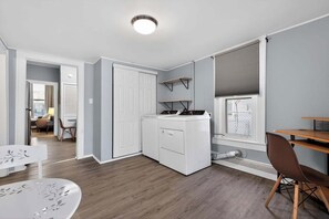 A compact hotel room with a washing machine, a dining area, and a view through a window. - Cozy Southfield Ranch (Southfield)