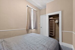 A bedroom with a bed, a window with curtains, and a closet with shelves. - Cozy Southfield Ranch (Southfield)