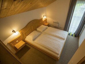 Ein Einzelbett mit einem Holz-Kopfteil und zwei Nachttischen, jeweils mit einer Lampe. Ein Heizkörper ist an der Wand sichtbar, und das Zimmer hat eine geneigte Decke.