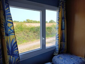 Una habitación con ventana que da a un paisaje rural, una cama con ropa de cama estampada y cortinas con diseño de hojas.
