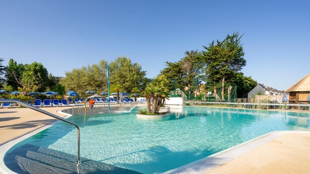 Ein klares Schwimmbecken mit Liegestühlen und Sonnenschirmen, umgeben von Bäumen und einem Gebäude.