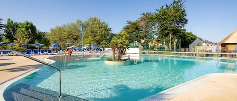 A clear swimming pool with lounge chairs and umbrellas, surrounded by trees and a building.