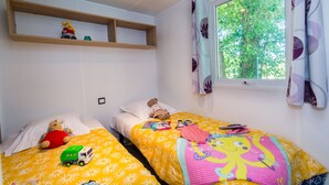 Ein Schlafzimmer mit zwei Betten, einem fenster mit Vorhängen, einem Regal mit Spielzeug und einem Teddybären auf einem Bett.