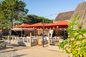 Een terras met tafels en stoelen, overdekt met rode parasols, omringd door groen.