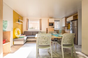 Un espacio habitable compacto con kitchenette, una zona de comedor con mesa y sillas, un sofá y una ventana con cortinas.