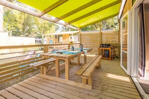 A wooden deck with picnic tables and a barbecue grill, surrounded by a wooden fence and trees. - Parc Aquatique | Proche de la plage | Plancha (Sarzeau)