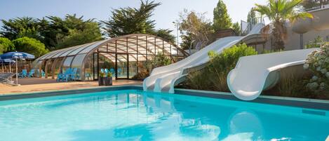 A swimming pool with a slide, surrounded by lounge chairs and a covered seating area.