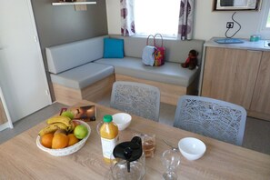 Et spiseområde med et bord dækket til to personer, en sofa og et vindue med gardiner.